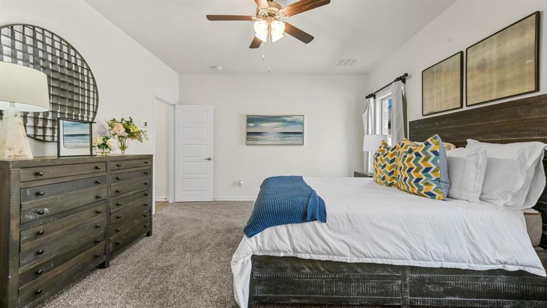 Spacious bedroom featuring plush gray carpeting, a multi-paneled door, and a ceiling fan