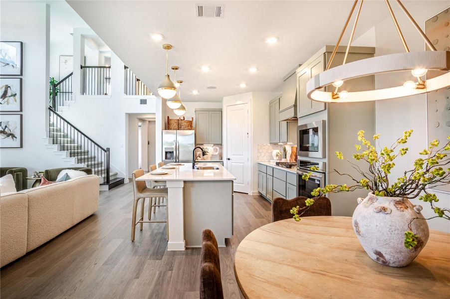 This photo showcases a modern, open-concept living space featuring a sleek kitchen with an island, stainless steel appliances, and stylish pendant lighting. Adjacent is a cozy living area with a staircase leading to the upper level, and a dining nook adorned with a decorative vase. The space is well-lit and inviting, with a contemporary design. This photo showcases a modern, open-concept living space featuring a sleek kitchen with an island, stainless steel appliances, and stylish pendant lighting. Adjacent is a cozy living area with a staircase leading to the upper level, and a dining nook adorned with a decorative vase. The space is well-lit and inviting, with a contemporary design.