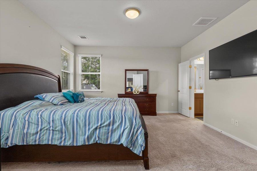 Carpeted floors and light-filled windows define this restful primary suite with an attached bathroom.