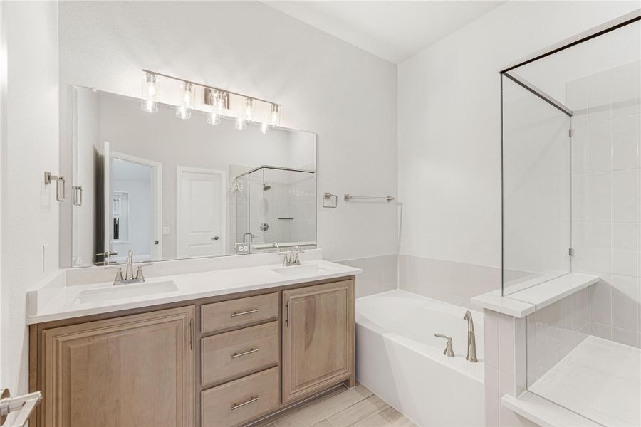 Bathroom with double vanity, wood cabinets, soaking tub, and glass shower enclosure