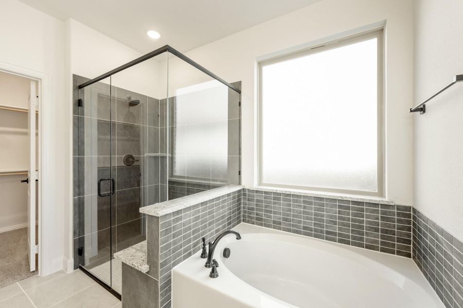 Master bathroom with soaking tub, glass-enclosed shower, gray tile surround, and walk-in closet access