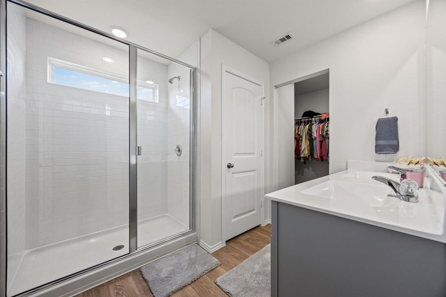 Full bathroom featuring a spacious closet, vanity, a stall shower, and light wood-style floors