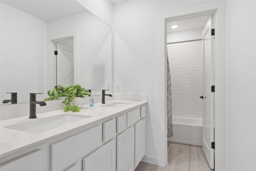 Bathroom with double vanity, shower / bath combo with shower curtain, and light wood-style floors