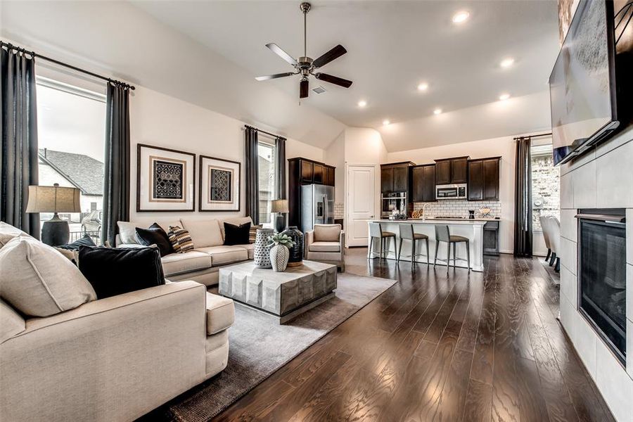 Living room with lofted ceiling, recessed lighting, dark wood-type flooring, a ceiling fan, and a tiled fireplace