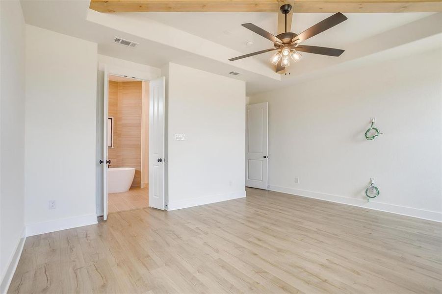 Unfurnished bedroom featuring light hardwood / wood-style flooring, ceiling fan, a raised ceiling, and ensuite bathroom