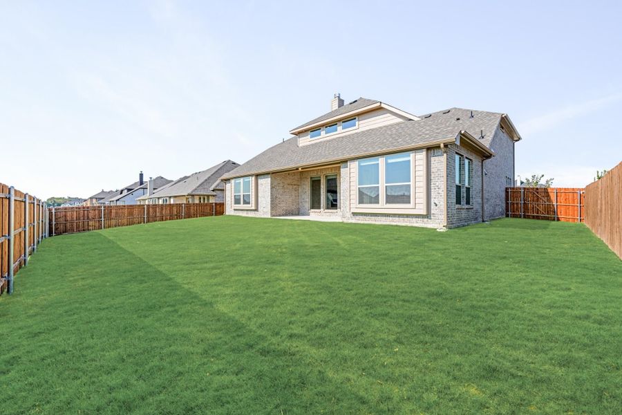 Brick home rear exterior with large fenced backyard and green lawn