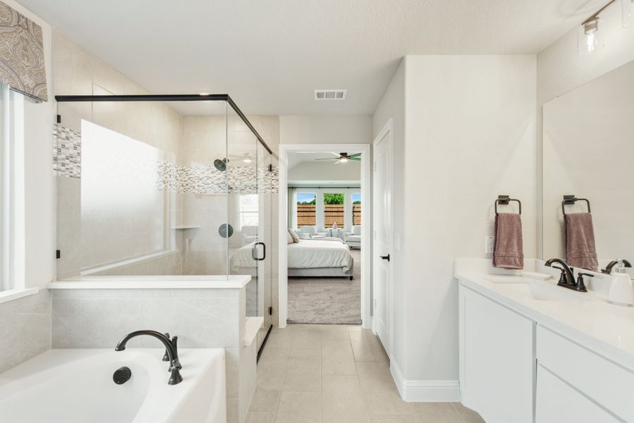 Master bathroom with soaking tub, glass walk-in shower, double vanity, and tile floors opening to bedroom
