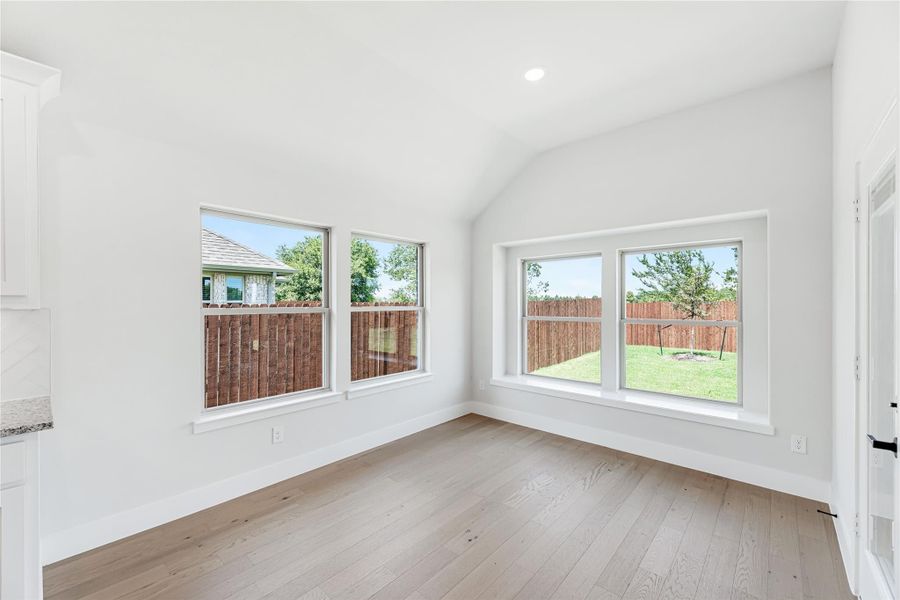 Bright empty room with vaulted ceiling, light wood floors, and four windows overlooking backyard