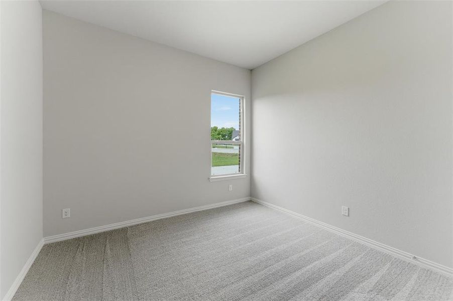 This room features light grey walls, grey carpet, and a window with a view of green landscaping