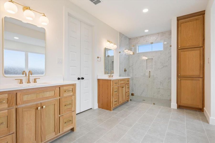Full bath featuring two vanities, a marble finish shower, light tile patterned flooring, and recessed lighting