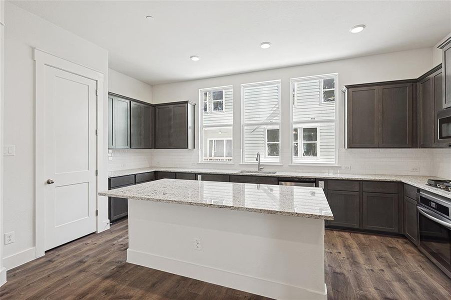 Kitchen with light stone countertops, dark hardwood / wood-style flooring, stainless steel appliances, sink, and a kitchen island