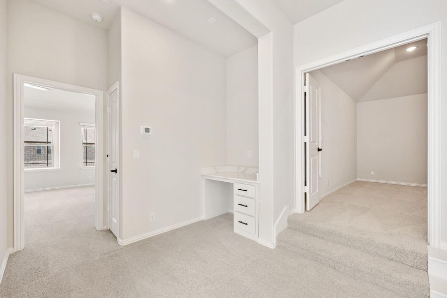 Empty bedroom with built-in desk, carpet flooring, and open walk-in closet with vaulted ceiling Empty bedroom with built-in desk, carpet flooring, and open walk-in closet with vaulted ceiling