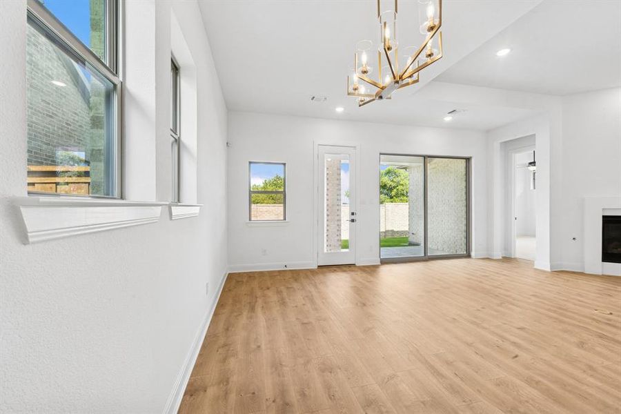 Unfurnished living room with light wood-style flooring, a glass covered fireplace, and a chandelier Unfurnished living room with light wood-style flooring, a glass covered fireplace, and a chandelier