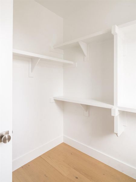 Walk-in closet featuring light wood-finish flooring, white walls, white baseboards, and built-in white shelving