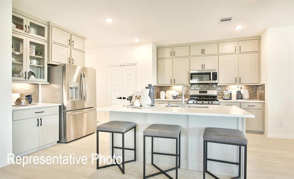 Contemporary kitchen featuring an island with seating, stainless steel appliances, light cabinetry, a subway tile backsplash, and recessed lighting