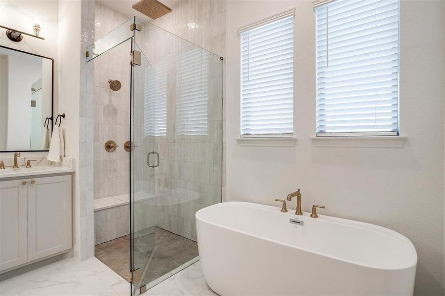 Primary Bathroom featuring vanity with dual sinks, gold hardware, tile flooring, garden tub and walk in shower with two shower heads including rain fall.