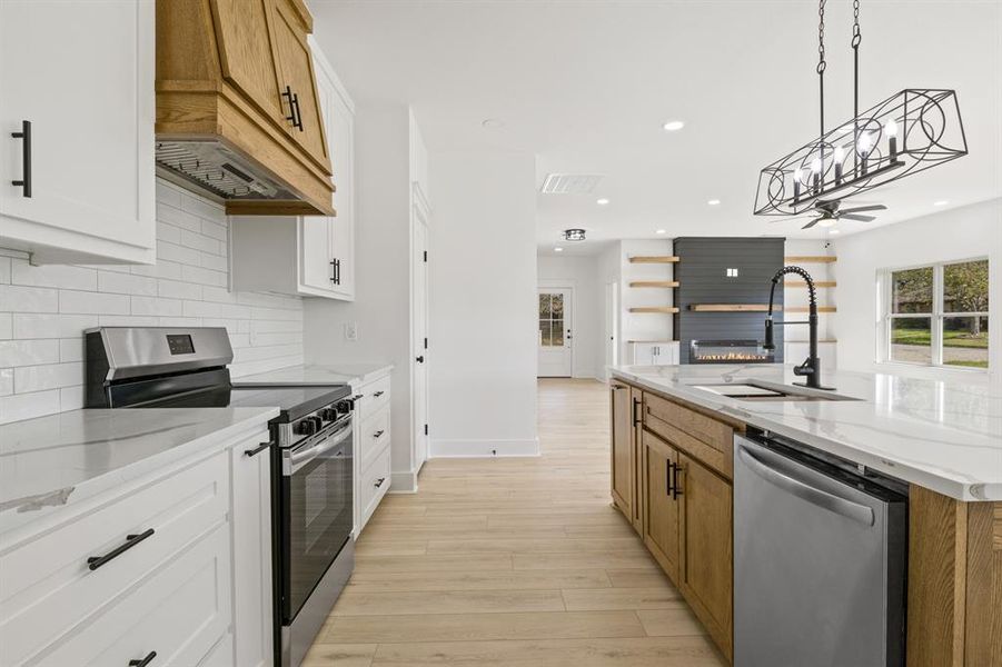 Kitchen featuring stainless steel appliances, light stone countertops, a large fireplace, hanging light fixtures, and recessed lighting