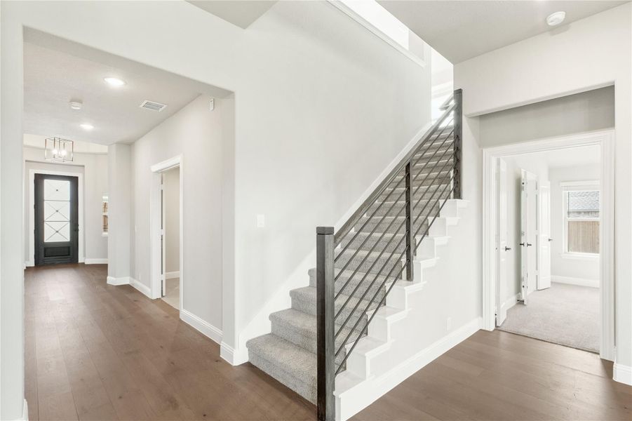 Entryway and staircase with dark wood floors, metal railing, and black front door visible down the hallway Entryway and staircase with dark wood floors, metal railing, and black front door visible down the hallway