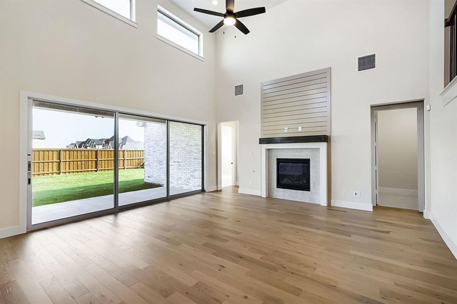 Unfurnished living room with healthy amount of natural light, a ceiling fan, a fireplace, a high ceiling, and light wood-type flooring Unfurnished living room with healthy amount of natural light, a ceiling fan, a fireplace, a high ceiling, and light wood-type flooring