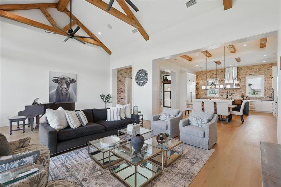 Living room with brick wall, light wood-style floors, beamed ceiling, ceiling fan, and high vaulted ceiling Living room with brick wall, light wood-style floors, beamed ceiling, ceiling fan, and high vaulted ceiling
