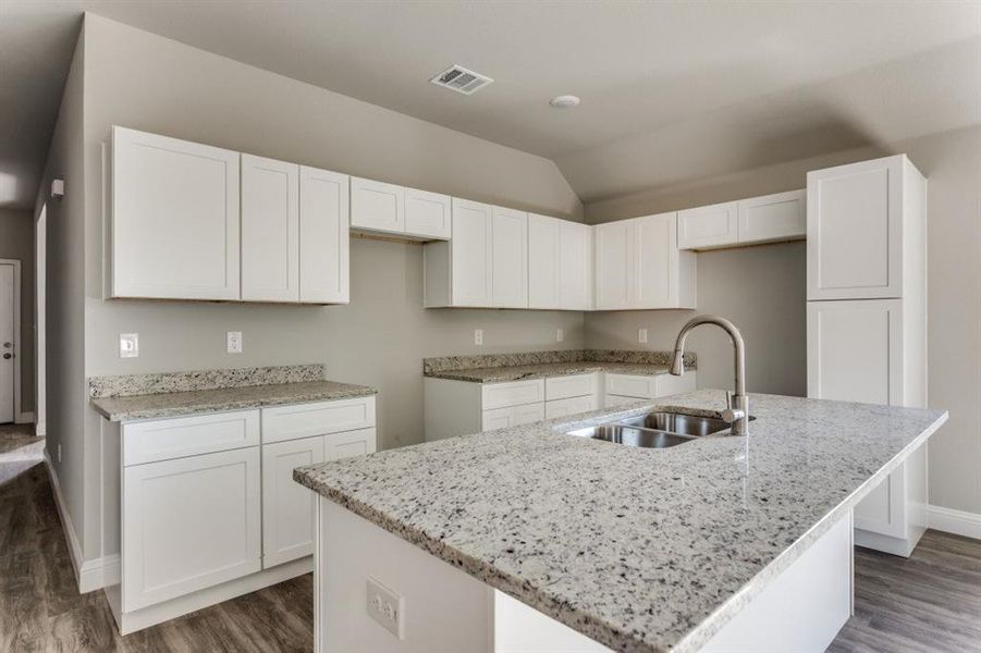 Kitchen with white cabinetry, dark wood-type flooring, light stone counters, vaulted ceiling, and an island with sink