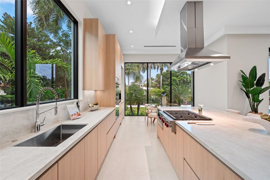 Gourmet kitchen with sleek custom cabinetry, waterfall island, premium appliances, and expansive windows framing lush tropical views. Gourmet kitchen with sleek custom cabinetry, waterfall island, premium appliances, and expansive windows framing lush tropical views.