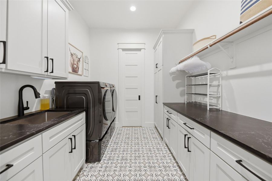 A well-appointed laundry room features ample counter space, custom cabinetry, a sink and modern appliances.
