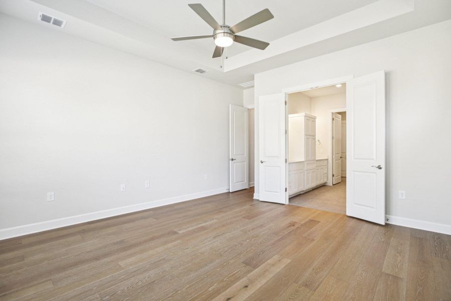 Unfurnished bedroom featuring light wood-type flooring, a ceiling fan, a raised ceiling, and ensuite bathroom