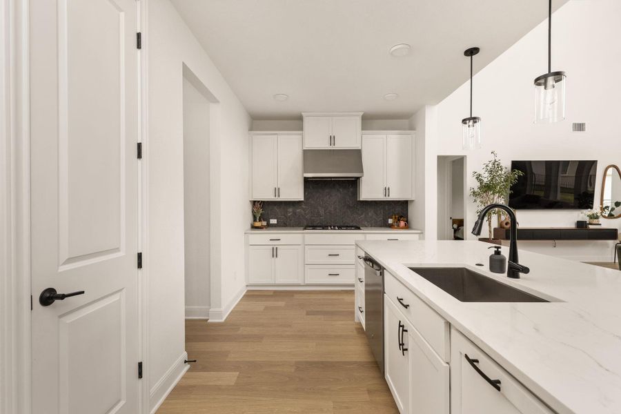 Modern kitchen featuring an expansive island with an integrated sink, white cabinetry, dark stone-finish backsplash, stainless steel appliances, and wood-finish flooring