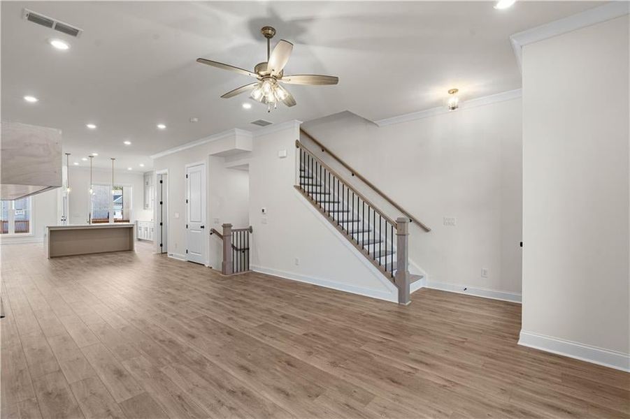 Unfurnished living room with recessed lighting, crown molding, light wood finished floors, ceiling fan, and stairway