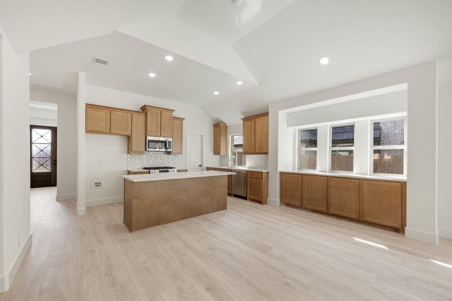 Open kitchen with wood cabinets, center island, stainless appliances, and light hardwood floors