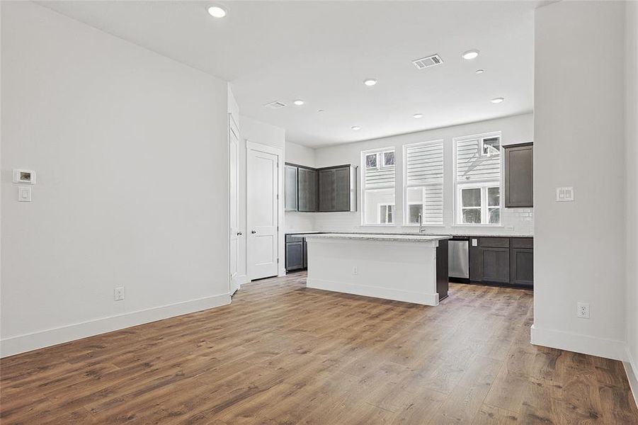 Kitchen with light stone countertops, a center island, stainless steel dishwasher, dark hardwood / wood-style floors, and dark brown cabinets