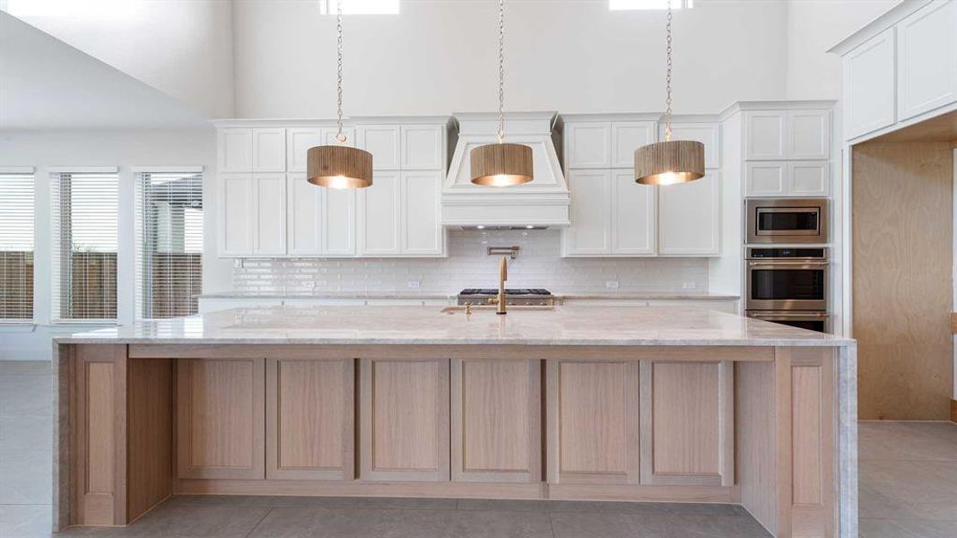 Kitchen with a center island with sink, light stone countertops, stainless steel microwave, and white cabinetry