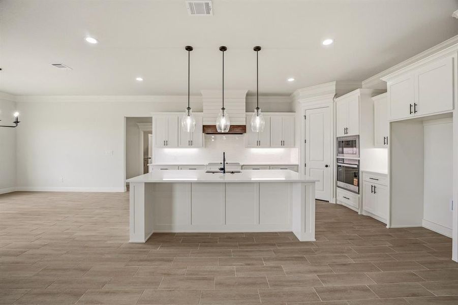 Kitchen featuring white cabinets, an island with sink, stainless steel appliances, wood tiled floors, and ornamental molding