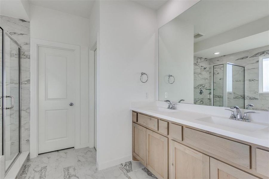 Full bath with a marble finish shower, double vanity, and light marble finish floors Full bath with a marble finish shower, double vanity, and light marble finish floors
