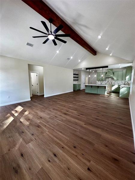 Open-concept living area with wood-finish flooring, vaulted ceilings, and an exposed wood beam