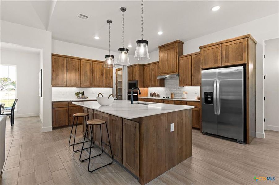 Kitchen with brown cabinetry, a kitchen island with sink, a breakfast bar, appliances with stainless steel finishes, and recessed lighting
