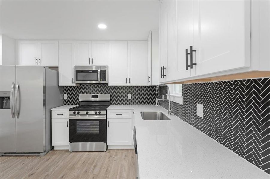 Kitchen with white cabinetry, light stone counters, stainless steel appliances, light wood-type flooring, and sink