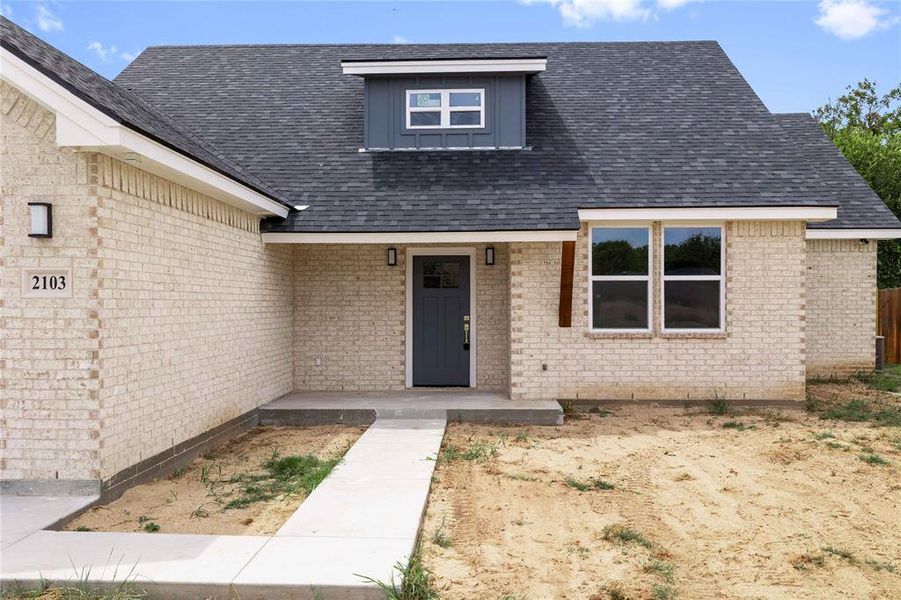 Entrance to property featuring brick siding, covered porch, and roof with shingles Entrance to property featuring brick siding, covered porch, and roof with shingles