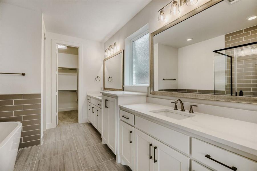 Bathroom with a spacious closet, a stall shower, a freestanding bath, two vanities, and tile walls