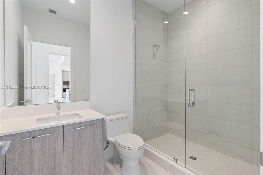 Bathroom featuring a vanity with a white countertop and rectangular undermount sink, a frameless glass-enclosed shower with floor-to-ceiling tile, and chrome fixtures