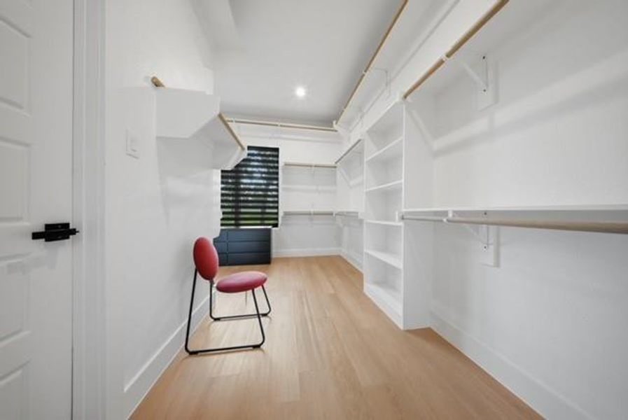 Spacious walk-in closet featuring light wood-finish flooring, recessed lighting, and extensive built-in shelving with hanging rods
