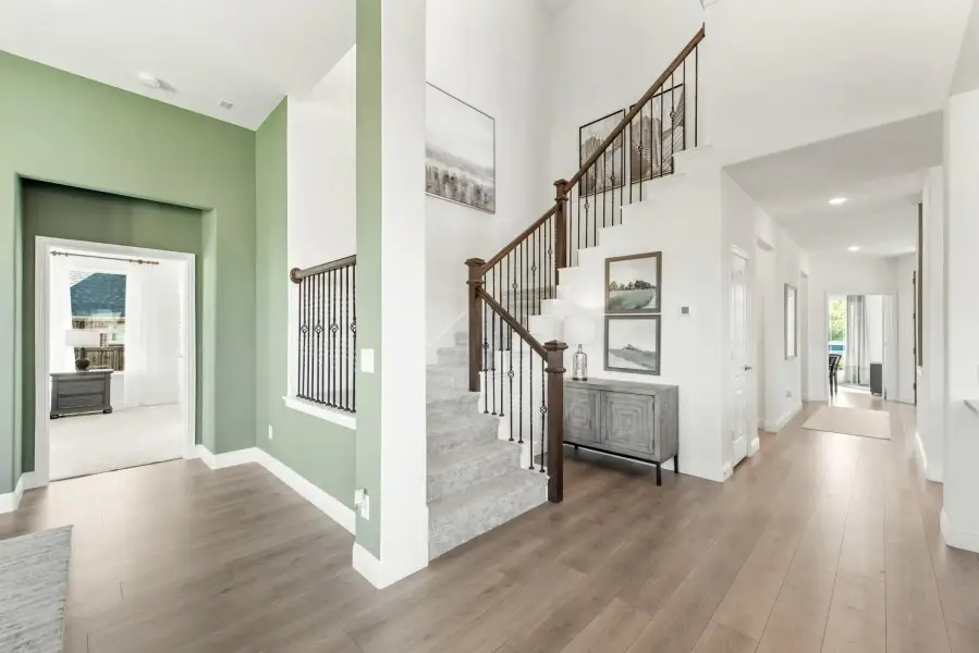 Two-story foyer with curved staircase, wood and iron railing, green accent walls, and hardwood floors