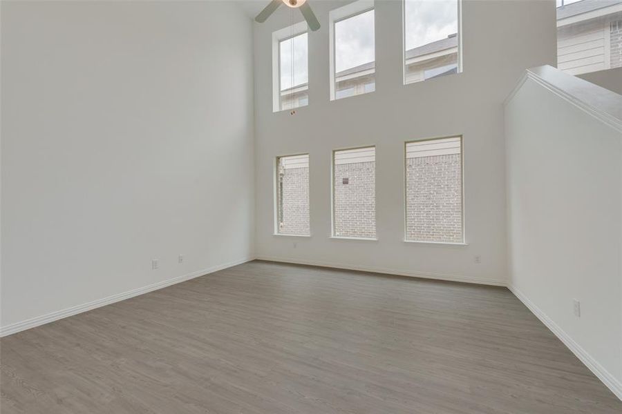 Unfurnished living room featuring ceiling fan, a towering ceiling, and light hardwood / wood-style flooring