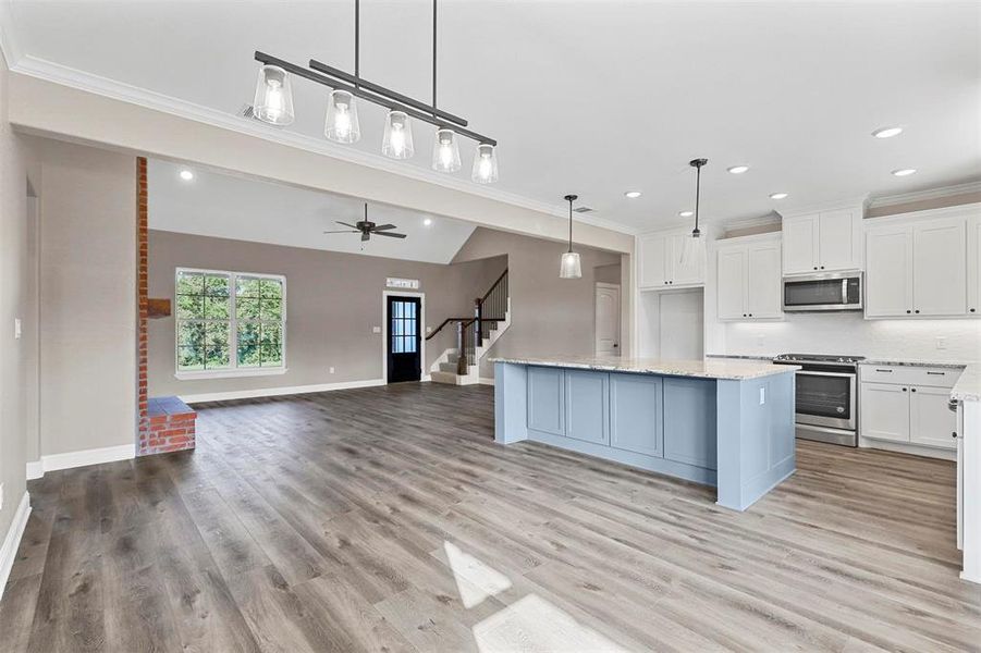 Kitchen with pendant lighting, ceiling fan, appliances with stainless steel finishes, white cabinets, and a center island