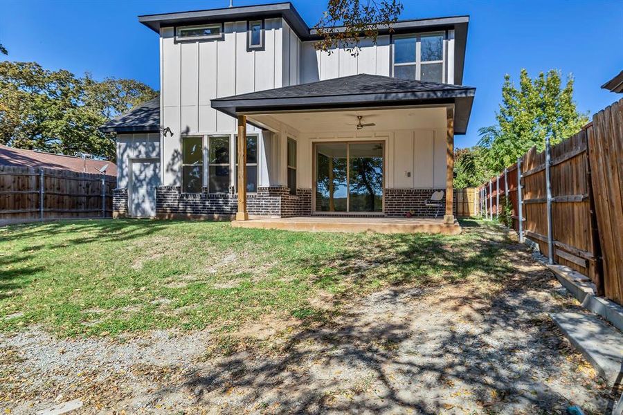 Rear view of property with board and batten siding, brick siding, a fenced backyard, a patio area, and a shingled roof