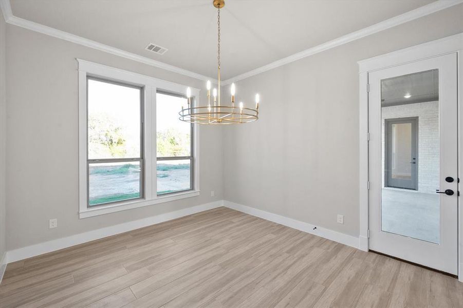 Spare room with light hardwood / wood-style flooring, ornamental molding, and a notable chandelier