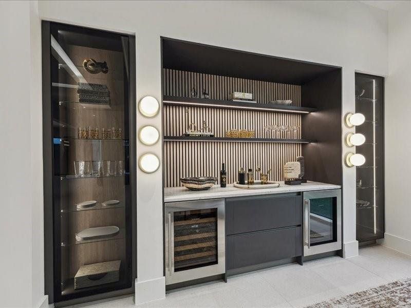 A sleek, high-end wet bar with dual glass towers elegantly displaying art and glassware, complete with a mini fridge and wine cooler for effortless entertaining.