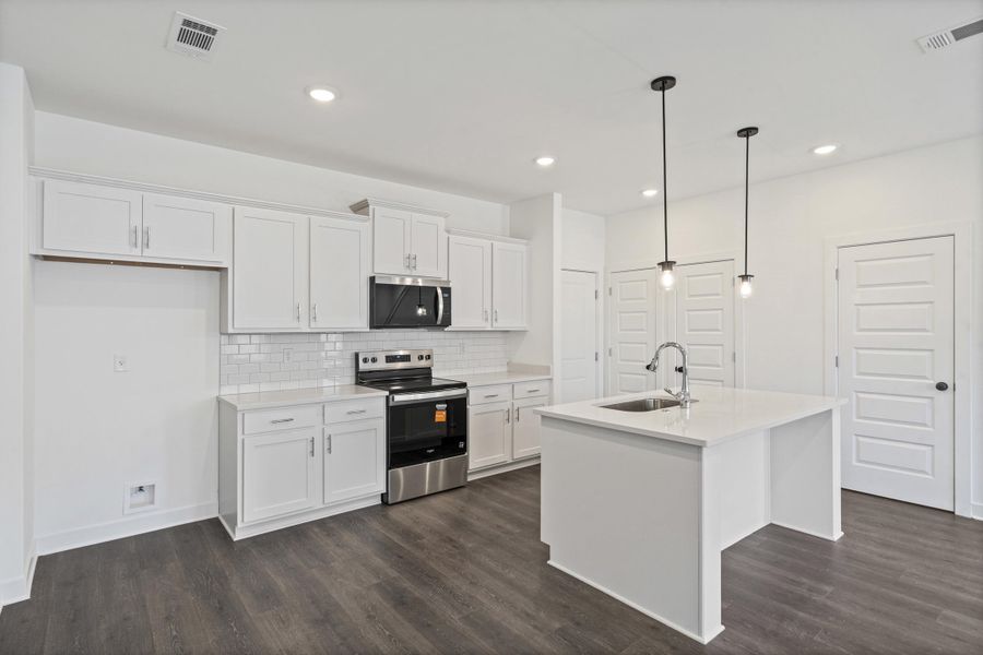 Contemporary kitchen featuring white cabinetry, subway tile backsplash, stainless steel appliances, and an island with a built-in sink