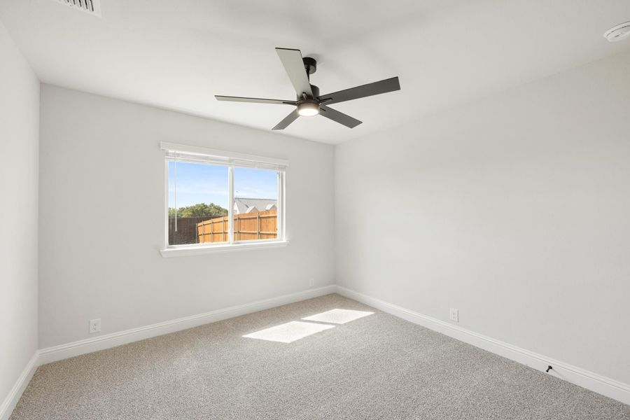 Empty bedroom with carpet flooring, ceiling fan, and a window overlooking a wood fence